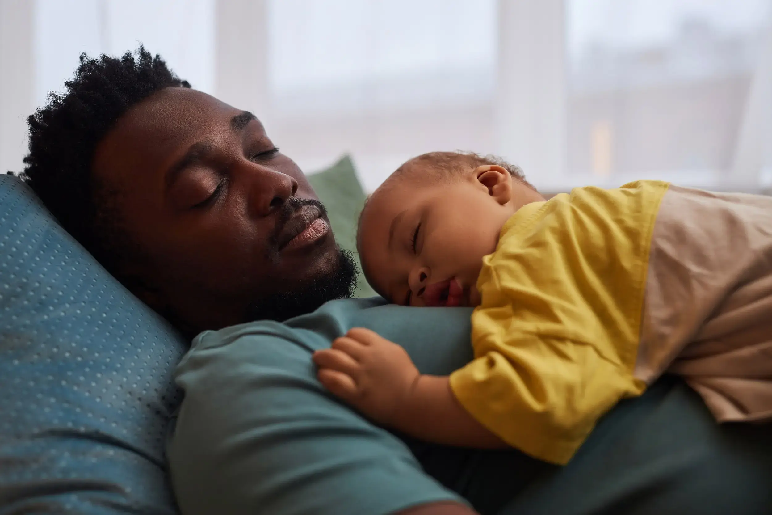 A father is napping with his baby son on his chest