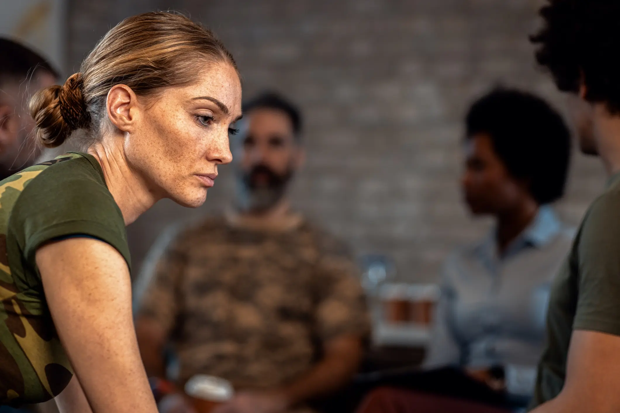 Woman in a camouflage pattern shirt looking down solemnly
