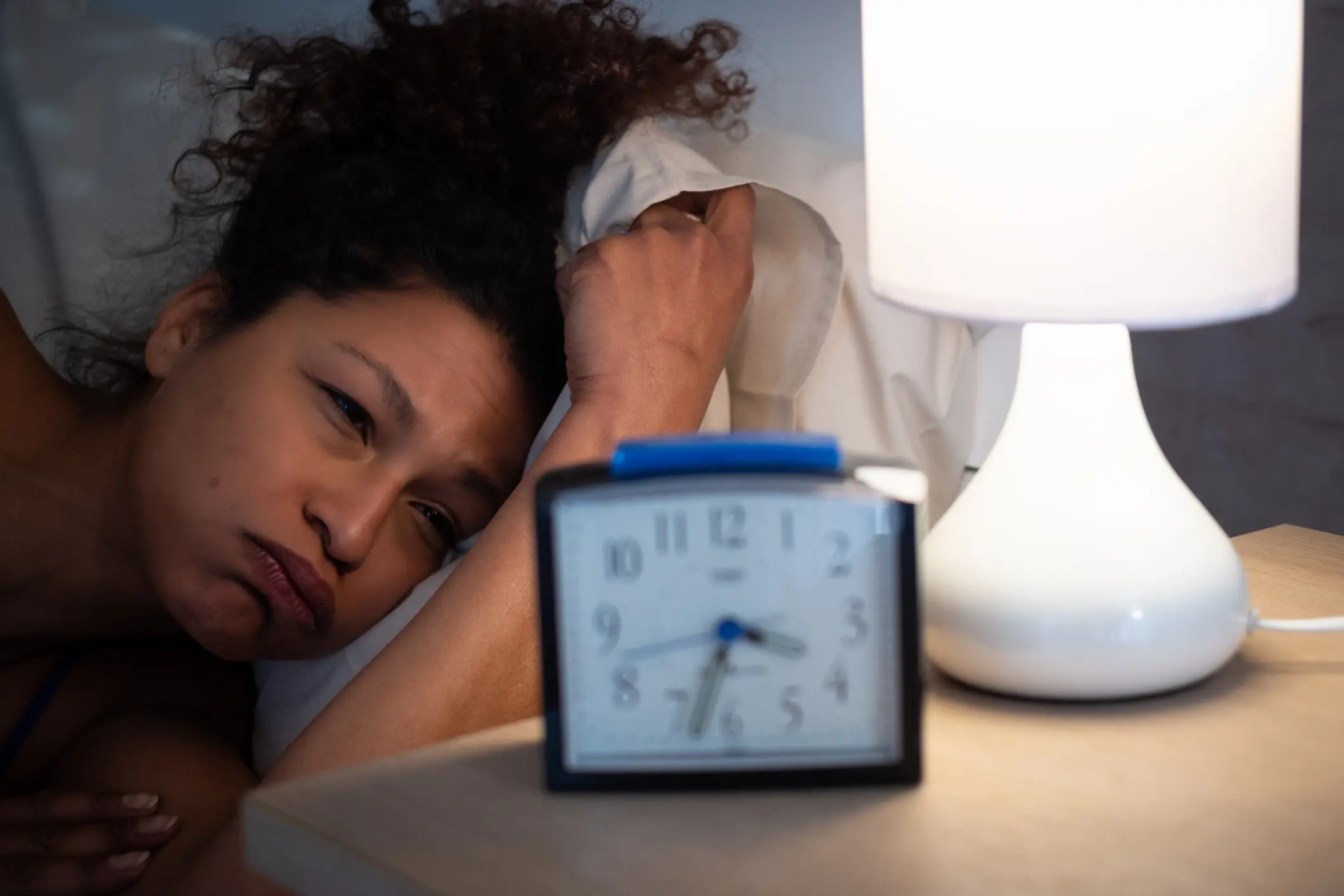 A woman waking up to her alarm clock unhappily